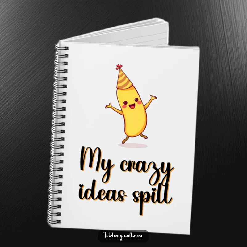 Funny dancing banana wearing a party hat slipping on its own peel on a spiral-bound notebook.